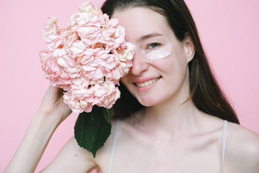 Best-Eye-Care-Routine-Cheerful woman with skincare cream and hydrangea against pink background, conveying natural beauty.